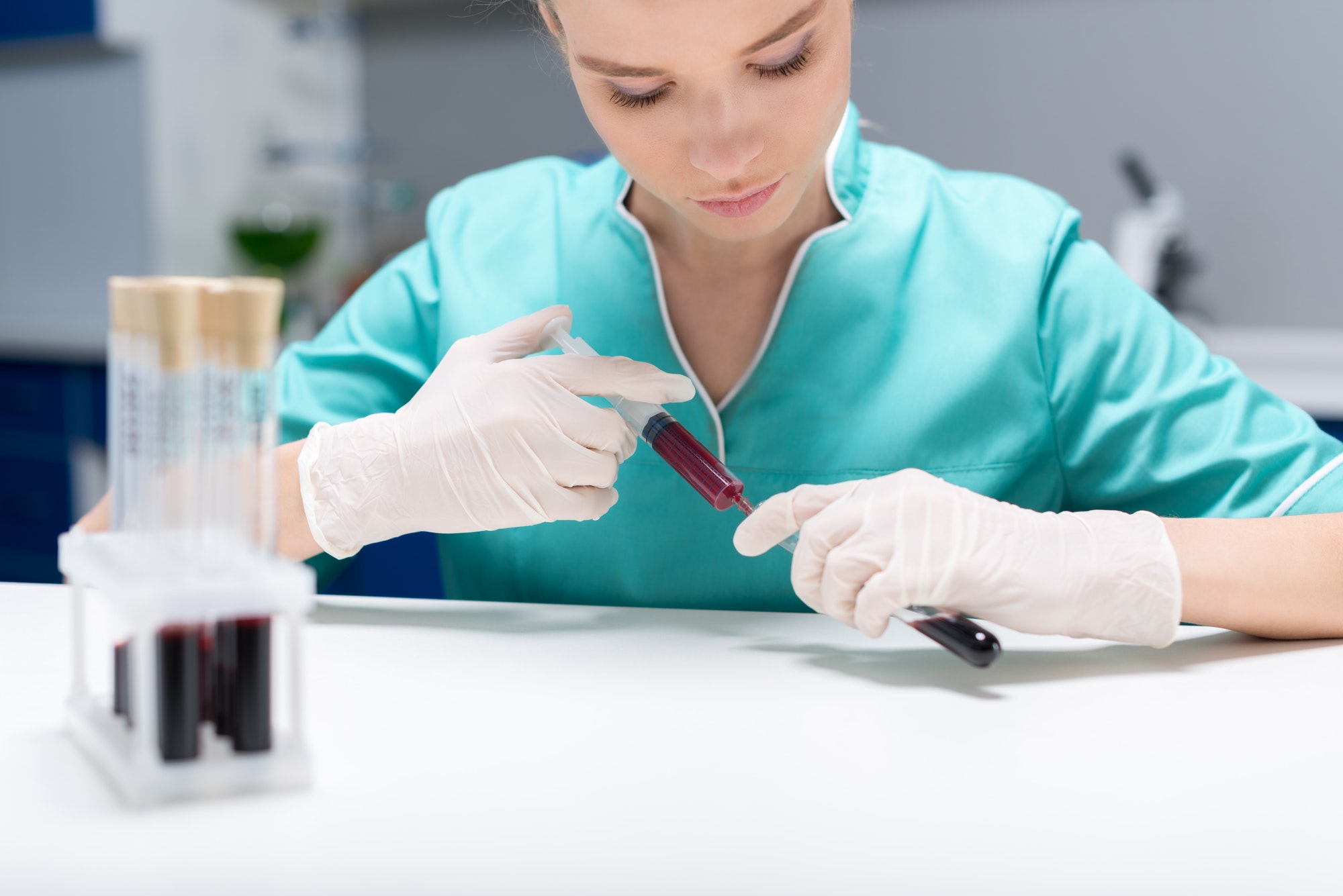 Nurse pouring blood samples from syringe into tubes at laboratory