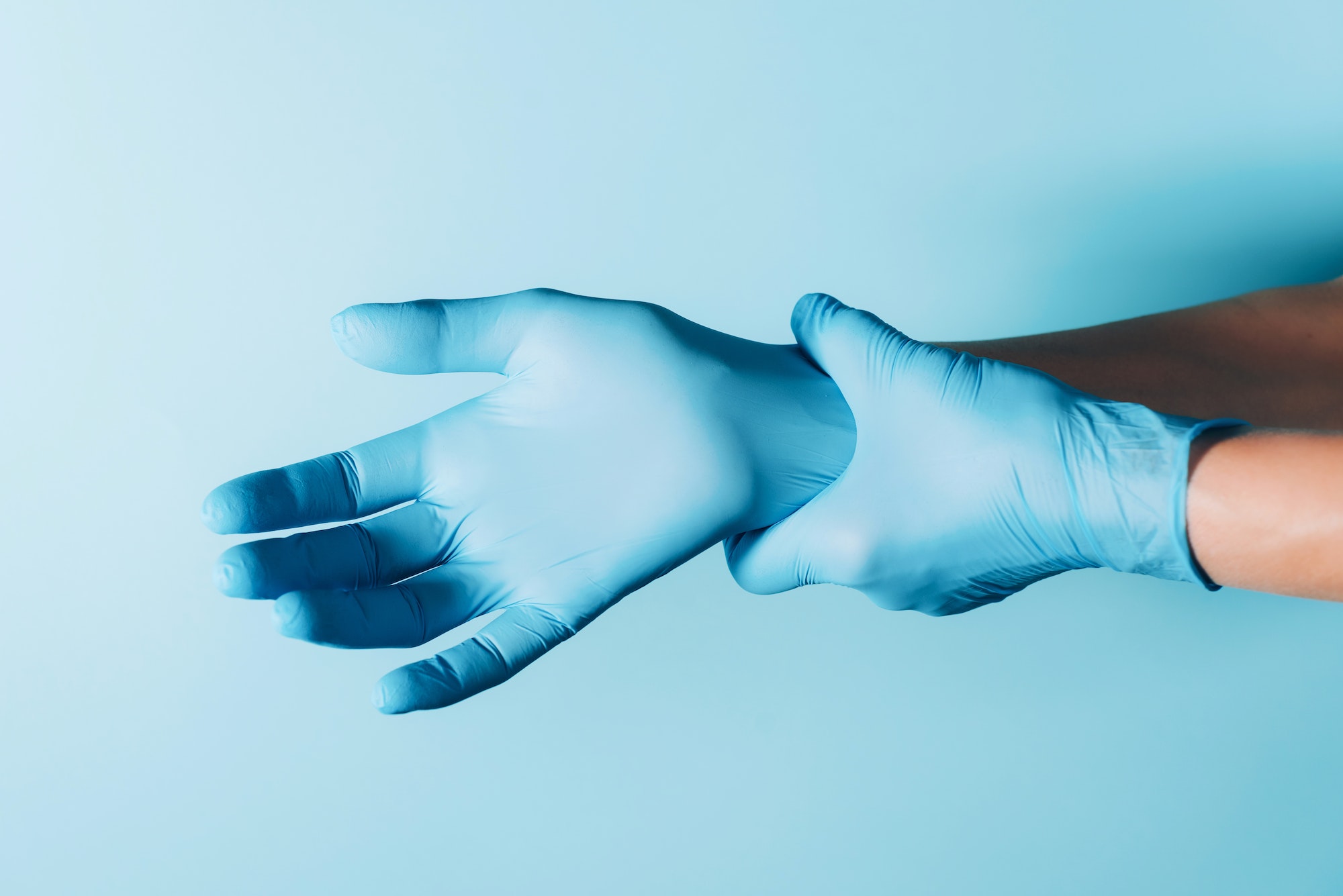 Doctor wears blue sterilized surgical gloves on blue background. Copy space. National Doctors'